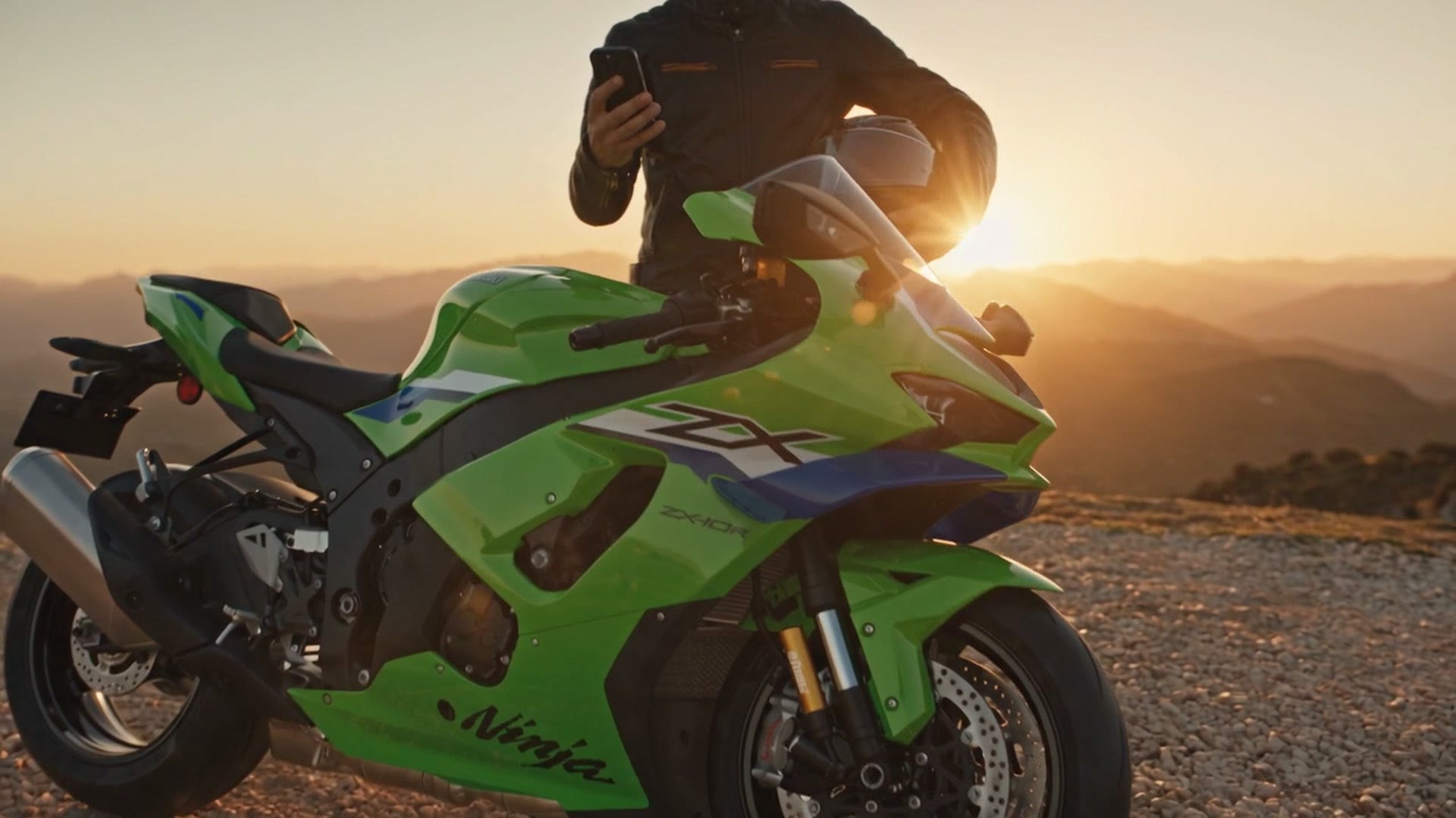 Una sportiva verde ferma sulla ghiaia al tramonto, con il motociclista in piedi dietro