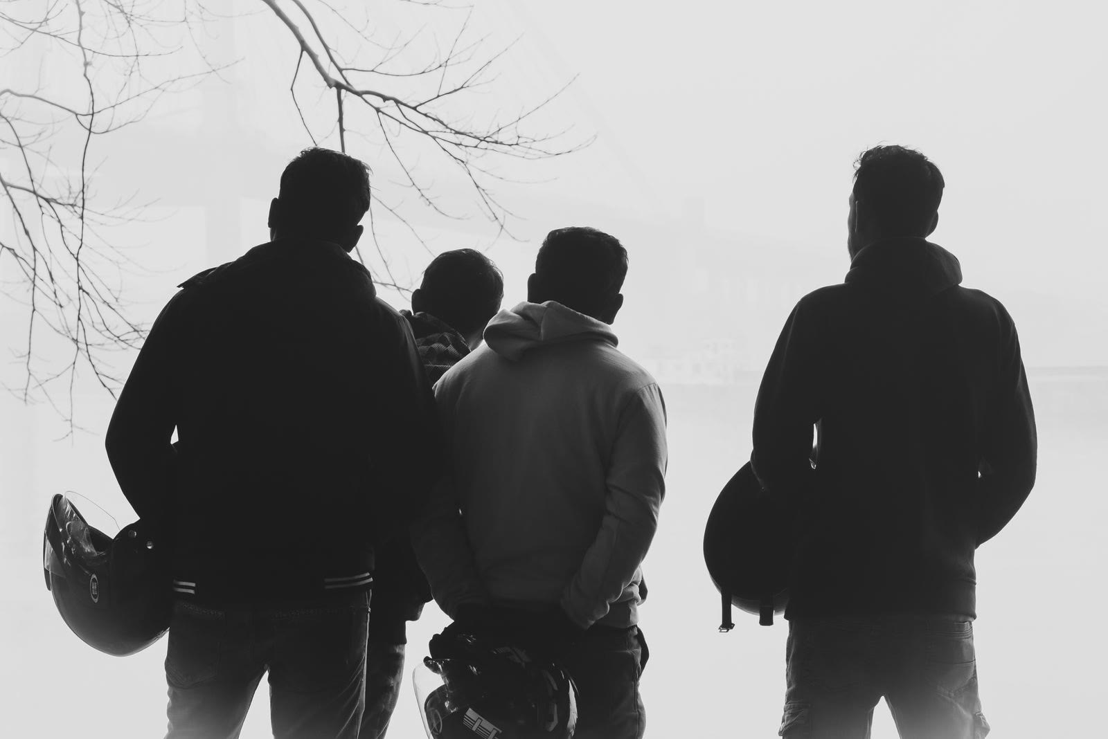 Quattro amici di spalle con i caschi in mano, nella foschia