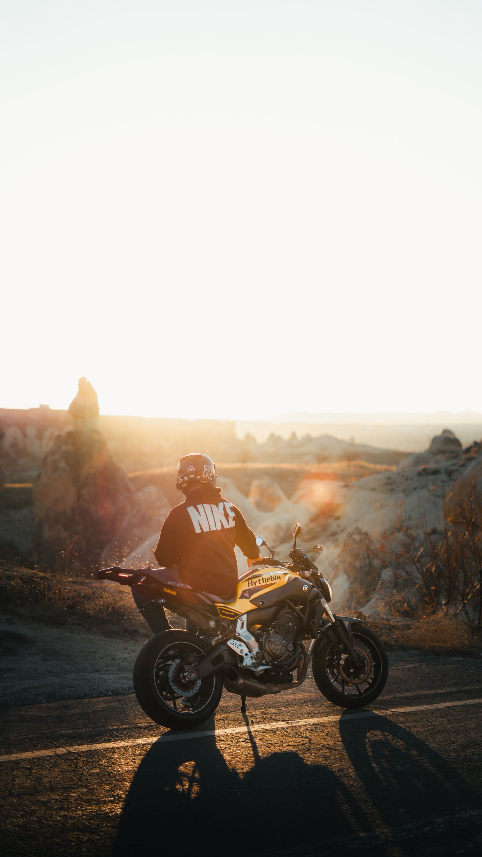 Un motociclista seduto sulla moto guarda il paesaggio al tramonto