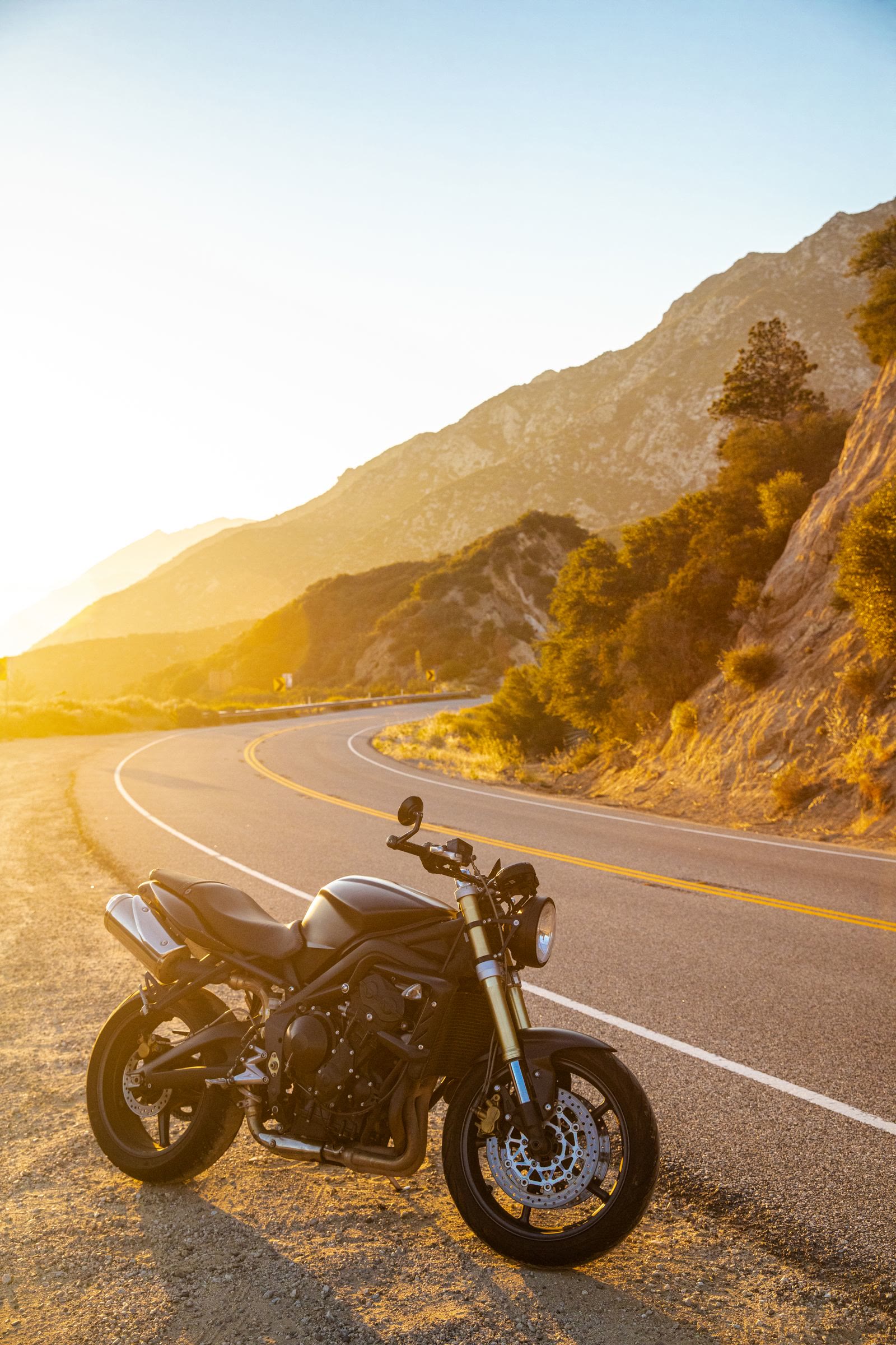 Una moto ferma sul ciglio di una strada di montagna, nella luce bassa del tramonto